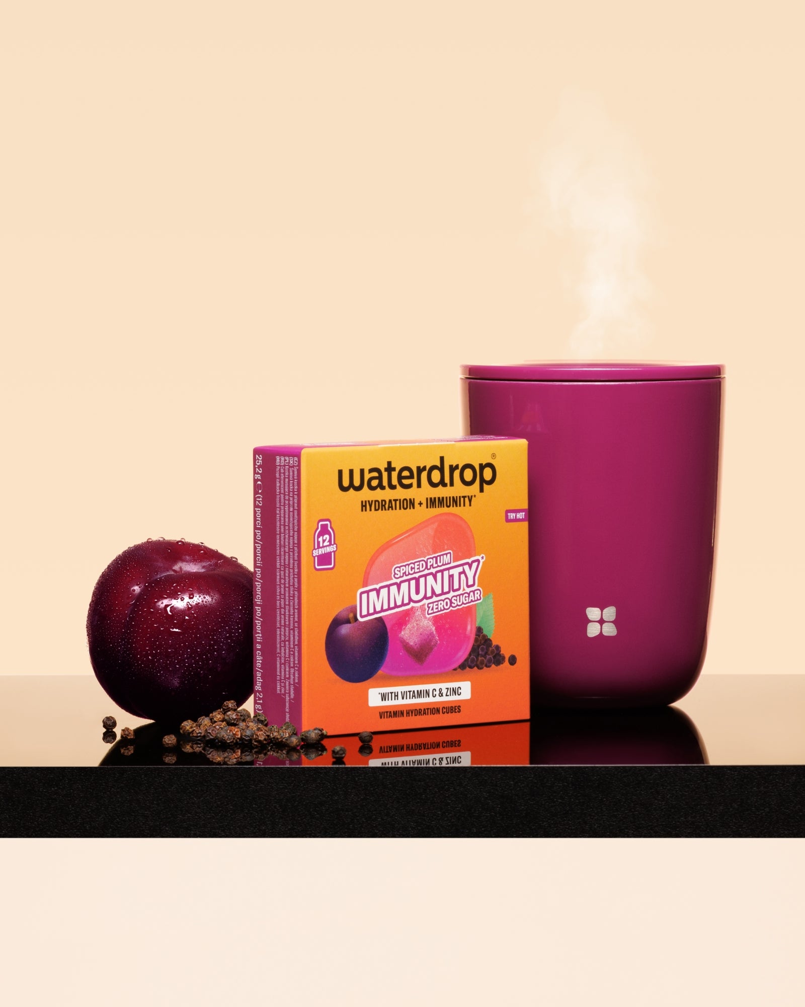 Кутија Waterdrop имуност за поддршка со слiвa и розова чаша со пар на црна површина.